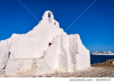 Famous tourist landmark, Mykonos, Greece. White Greek Orthodox church of Panagia Paraportiani, town of Chora on island at sunrise. Iconic destination 80340547