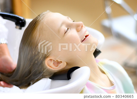 Portrait of a beautiful little girl in the hairdresser. Washing your hair with pleasure 80340665