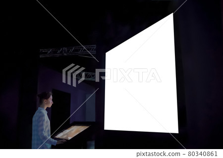 Woman using kiosk and looking at large blank white screen in dark room Woman using kiosk and looking at large blank white screen in dark room 80340861