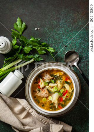 Hot delicious beef soup. Homemade soup with meat, vegetables and gnocchi on a dark stone background. Top view flat lay. Copy space. 80340869