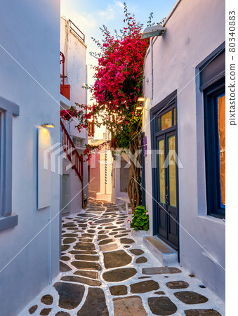 Beautiful traditional narrow cobbled alleys of Greek island towns. Whitewashed houses, shops, morning summer sunshine, bougainvillea, Mykonos, Greece. 80340883