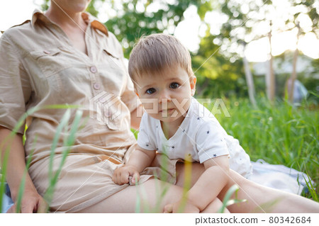 young mom hugs her little son while sitting in the park on the lawn 80342684