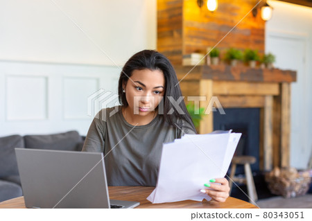 Asian woman works with documents in front of a laptop monitor. She checks the tax records before submitting the report. Asian woman works with documents in front of a laptop monitor. She checks the tax records before submitting the report. 80343051
