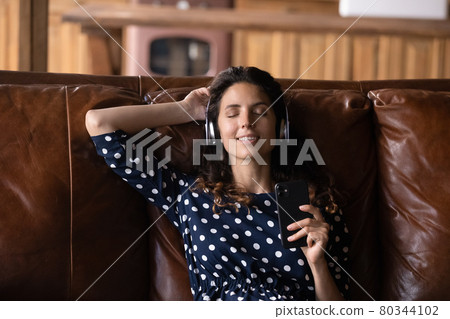 Happy tranquil Hispanic woman taking pause, enjoying lounge music 80344102
