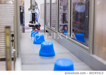Blue pots on conveyor belt of plastic injection molding machine with robotic arm 80345413