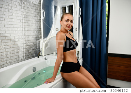 Beautiful young woman getting ready for spa beauty treatment in spa capsule. Hydro and vibromassage in a modern wellness spa Beautiful young woman getting ready for spa beauty treatment in spa capsule. Hydro and vibromassage in a modern wellness spa 80346152