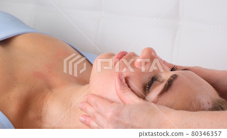 Facial massage beauty treatment. Close up of a young womans face lying on back, getting face lifting 80346357