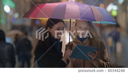 Female friends using touch pad on rainy evening in city Female friends using touch pad on rainy evening in city 80348286