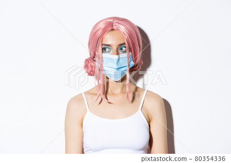 Close-up of young woman in pink wig and medical mask, social distancing during covid-19 pandemic, celebrating halloween with safety measures 80354336