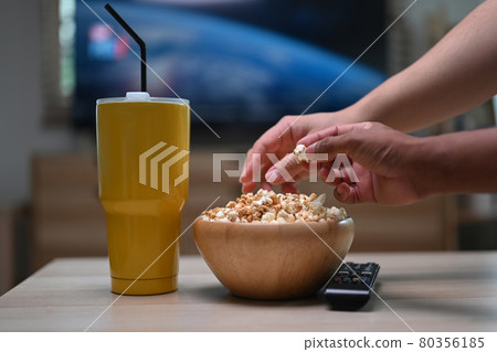 Cropped shot two man watching TV in living room and eating popcorn. 80356185