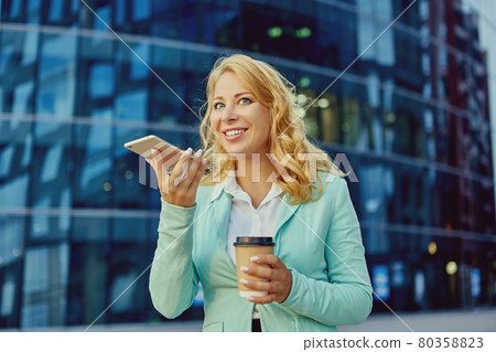 Young woman talks by cellphone and drinks coffee outside. 80358823