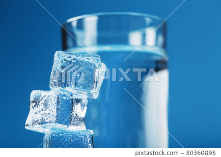 A glass of ice and clear water, ice cubes on a blue background. A glass of ice and clear water, ice cubes on a blue background. 80360898