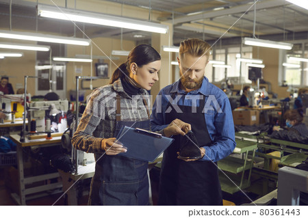 Female master with clipboard checking shoe for defect in shoemaker hands 80361443