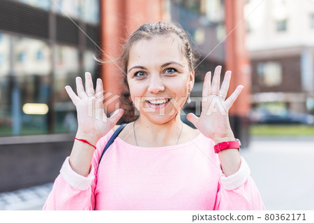 Portrait of enthusiastic young Caucasian woman raising her hands up on the street. Portrait of enthusiastic young Caucasian woman raising her hands up on the street. 80362171