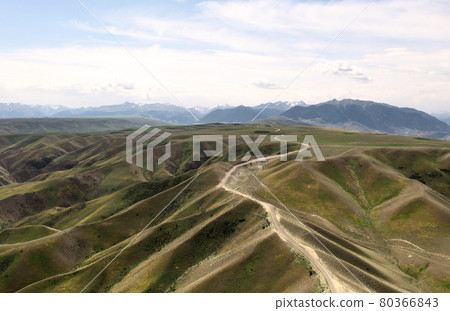 Mountain peaks and grassland are under white clouds. 80366843