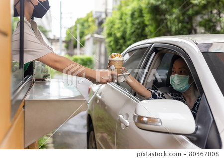 Woman customer in protective mask picking up cup of coffee at driving through. 80367008