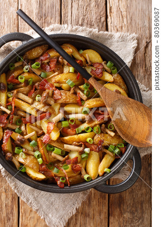 Fried potatoes with bacon and mushrooms close-up in a frying pan. Vertical top view 80369087