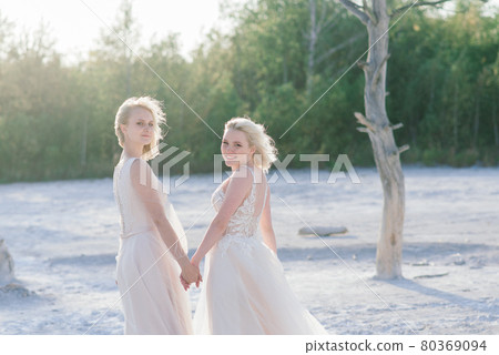Beautiful lesbian couple walking on sand along river bank on their wedding day Beautiful lesbian couple walking on sand along river bank on their wedding day 80369094