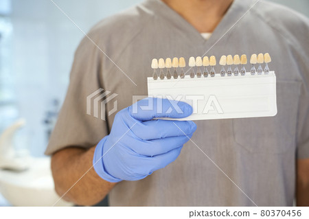Dentist posing with teeth-whitening kit in his office Dentist posing with teeth-whitening kit in his office 80370456