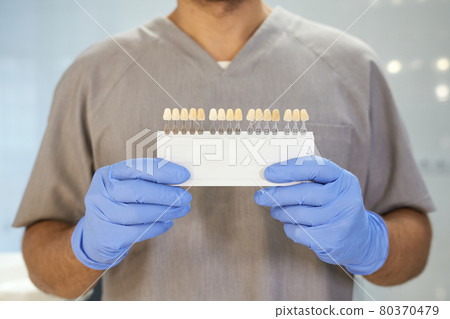 Dental specialist posing with set of color samples of teeth Dental specialist posing with set of color samples of teeth 80370479