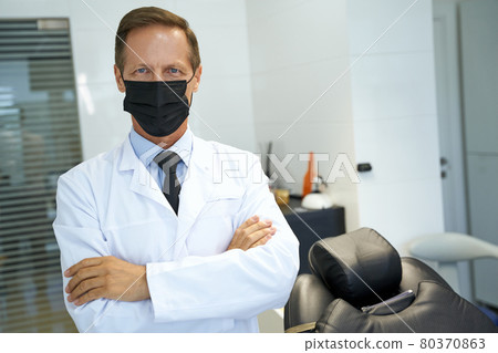 Qualified dental specialist posing while wearing a mask 80370863
