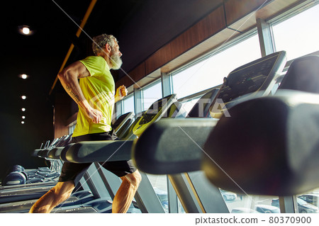 Side view of a athletic middle aged man in sportswear running on a treadmill in a gym, doing cardio before workout 80370900