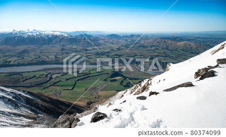 Beautiful view from top of snowy mountain down to green valley with mountains backdrop and blue sky. Shot in Mount Hutt, Canterbury Region,New Zealand 80374099