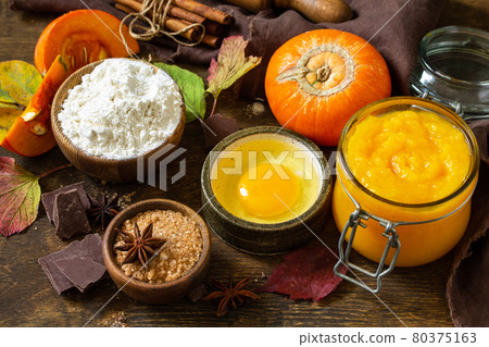 Seasonal food background - ingredients for autumn baking (pumpkin puree, eggs, flour, chocolate, sugar and spices) on a wooden table. 80375163