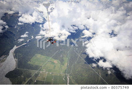 Skydiving in tandem,seconds after jumping out of plane, tilted shot with clouds in backdrop. Shot above Franz Josef Glacier in West Coast Region of NZ Skydiving in tandem,seconds after jumping out of plane, tilted shot with clouds in backdrop. Shot above Franz Josef Glacier in West Coast Region of NZ 80375749