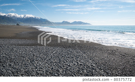 Remote beach with azure waters, blue skies and mountains in backdrop. Shot with waves coming in made in Kaikoura peninsula, New Zealand Remote beach with azure waters, blue skies and mountains in backdrop. Shot with waves coming in made in Kaikoura peninsula, New Zealand 80375772