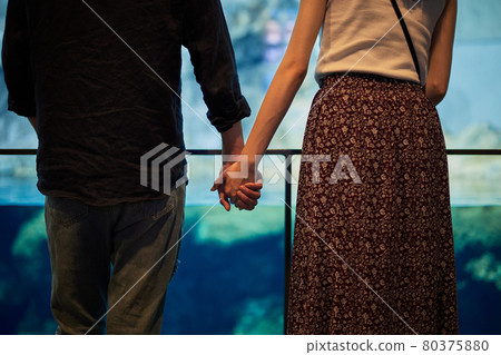 A young couple dating while holding hands in an aquarium A young couple dating while holding hands in an aquarium 80375880