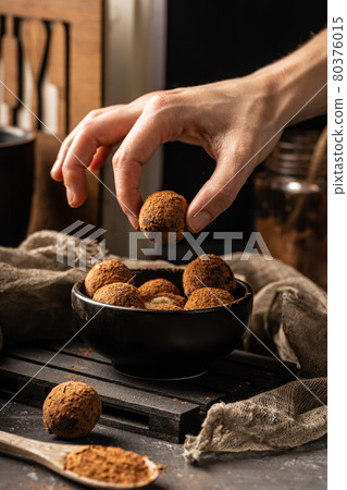 Woman hand take out a peace of homemade delicious cocoa ball with healthy ingredients from a black plate, covered with cocoa powder Woman hand take out a peace of homemade delicious cocoa ball with healthy ingredients from a black plate, covered with cocoa powder 80376015