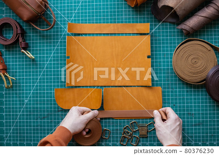 Process cutting scheme of bag with equipment and materials. Male tanner working at leather workshop Process cutting scheme of bag with equipment and materials. Male tanner working at leather workshop 80376230