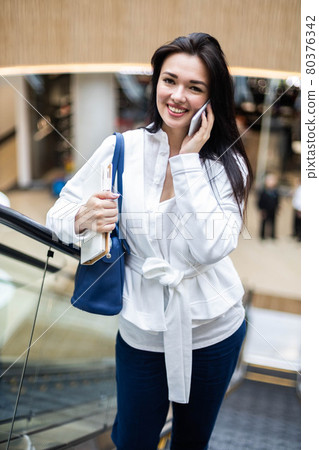 Cheerful business woman talking smartphone smiling having positive emotion at modern shopping mall Cheerful business woman talking smartphone smiling having positive emotion at modern shopping mall 80376342
