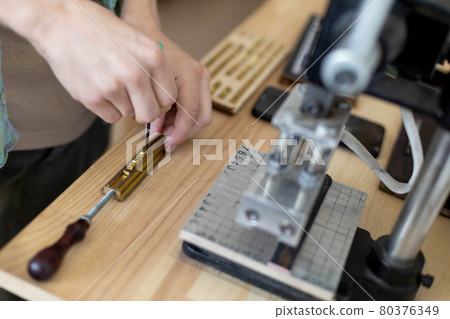 Closeup craftsman hands typing text for branding leather with personal stamp. Creating craft label Closeup craftsman hands typing text for branding leather with personal stamp. Creating craft label 80376349