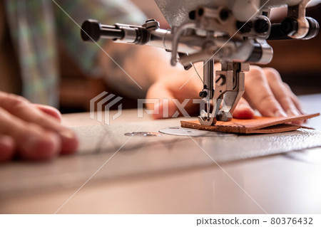 Close up craftsman hands sew stuff blank for wallet use sewing machine. Working at leather workshop 80376432