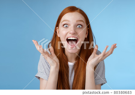 Excited overwhelmed young attractive female redhead fan go nuts thrilled wide eyes surprised yelling astonished receive exciting good news raise hands triumphing winning lottery extremely happy 80380683
