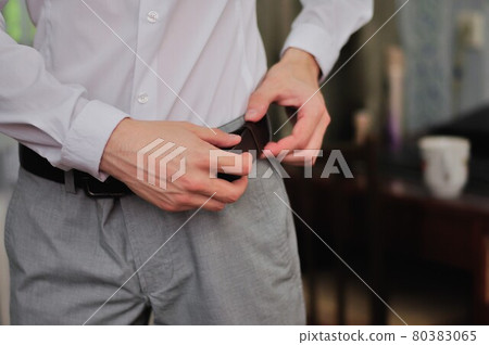 man fastens a belt on his trousers  80383065