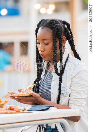 Afro american woman picking up a pizza slice at an outdoors terrace 80385607