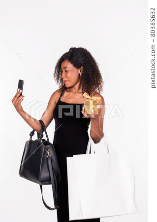 Afro American woman holding shopping bag, handbag and gift in hand and taking a selfie 80385632