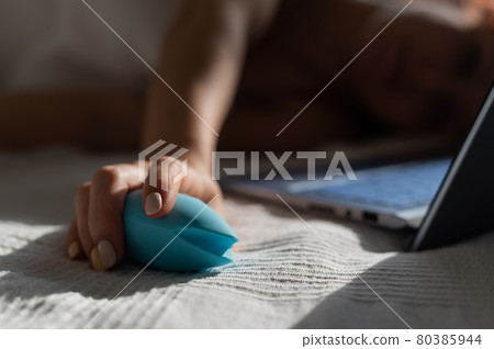 A woman lies in bed holding a clitoral vibrator and watching porn on a laptop. The girl has sex online 80385944