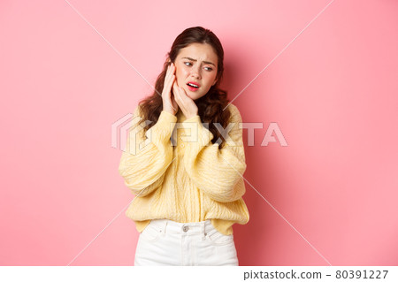 Young woman having toothache, touching swallen cheek and grimacing from pain, need to see dentist, stomatology appointment, standing against pink background Young woman having toothache, touching swallen cheek and grimacing from pain, need to see dentist, stomatology appointment, standing against pink background 80391227