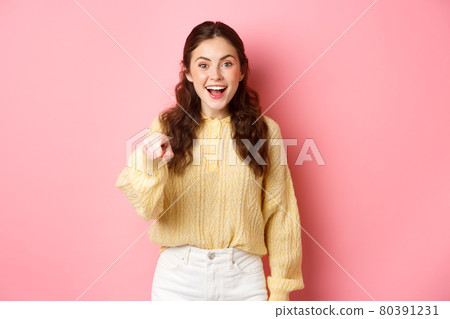Young brunette woman laughing, smiling amazed and pointing at camera, choosing you, standing against pink background Young brunette woman laughing, smiling amazed and pointing at camera, choosing you, standing against pink background 80391231