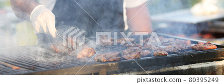 Gloved chef turns meat on grill with tongs Gloved chef turns meat on grill with tongs 80395249