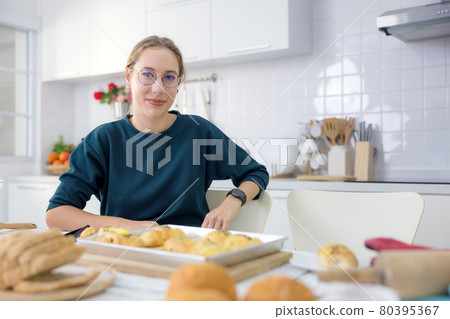 Making cakes and cookies is a lot of fun. In her kitchen, a young woman holds delicious fresh bread. 80395367