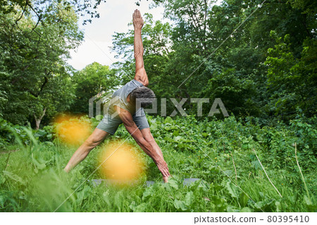 Man making bends and feeling flexible while exercising at the forest 80395410