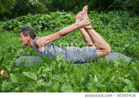 Man holding his legs with his hands while laying at the yoga mat at the flexible pose 80395416