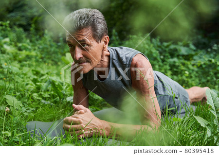 Man doing plank while standing at the yoga mat at the grass 80395418