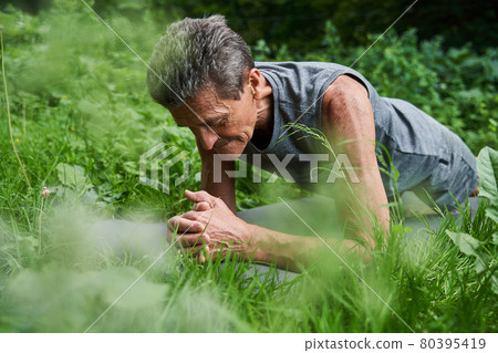 Serious retirement male engaging in sports activities on the yoga mat at the grass 80395419