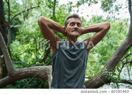 Man sitting at the tree trunk with closed eyes and keeping his hands behind the head 80395460